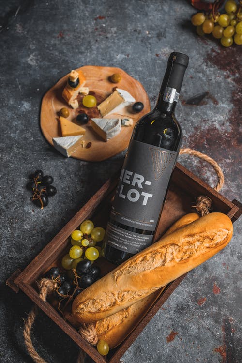 a wine bottle, bread, and grapes in a wooden box, a charcuterie board with different cheeses and grapes