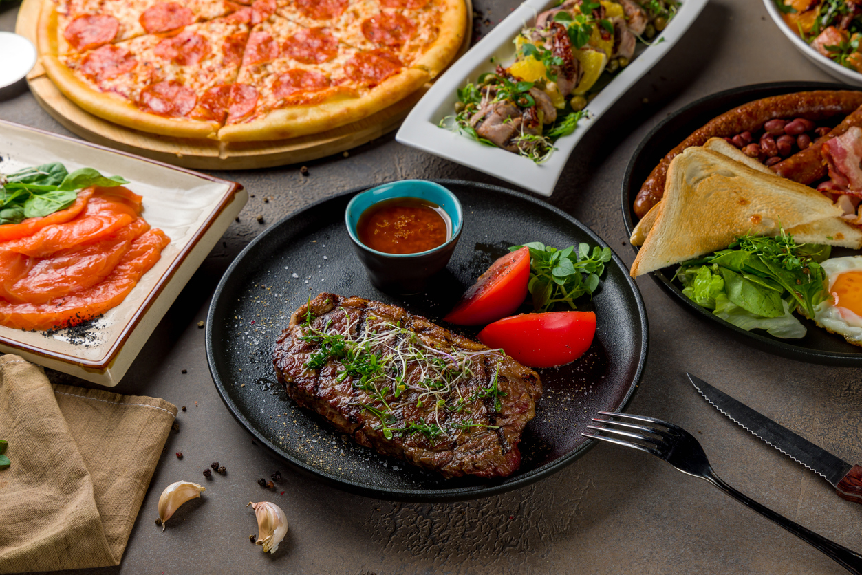 juicy striploin steak with tomato sauce and vegetables on black plate, English breakfast, salted salmon, salad with duck and pizza pepperoni