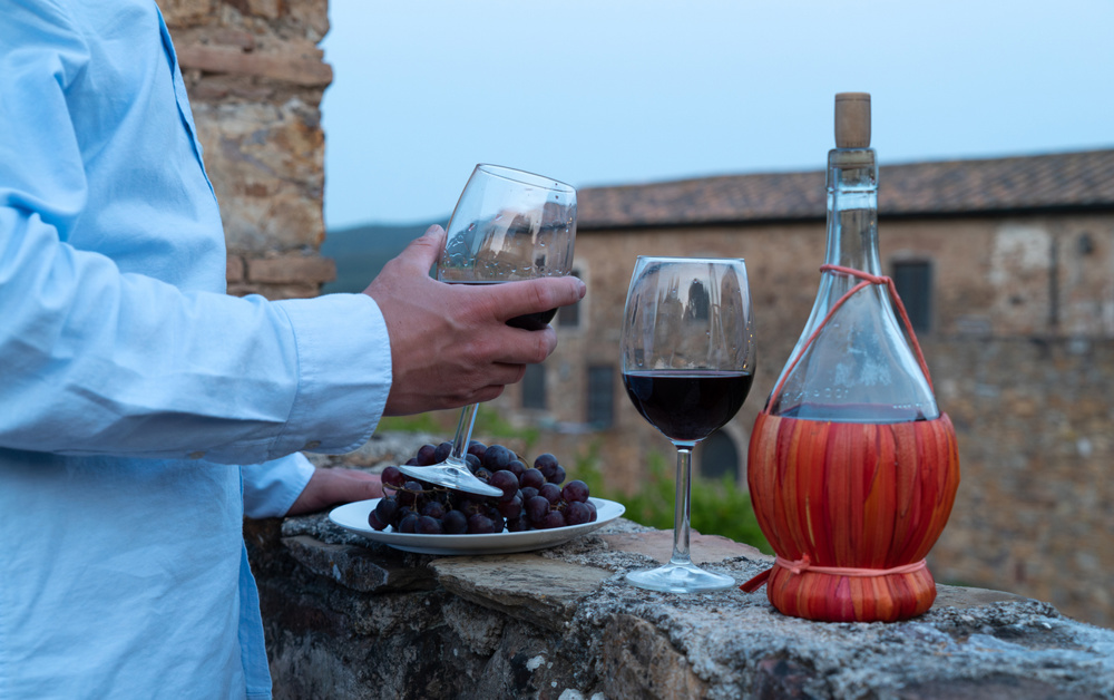 Italy, Tuscany. Man testing red wine from the typical chianti wine bottle fiasco against the backdrop of the Tuscany landscape