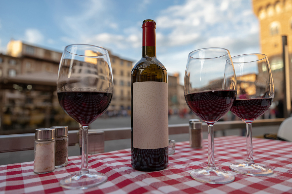 Closeup of bottle red wine and glasses on table of restaurant on background of Piazza della Signoria in summer day