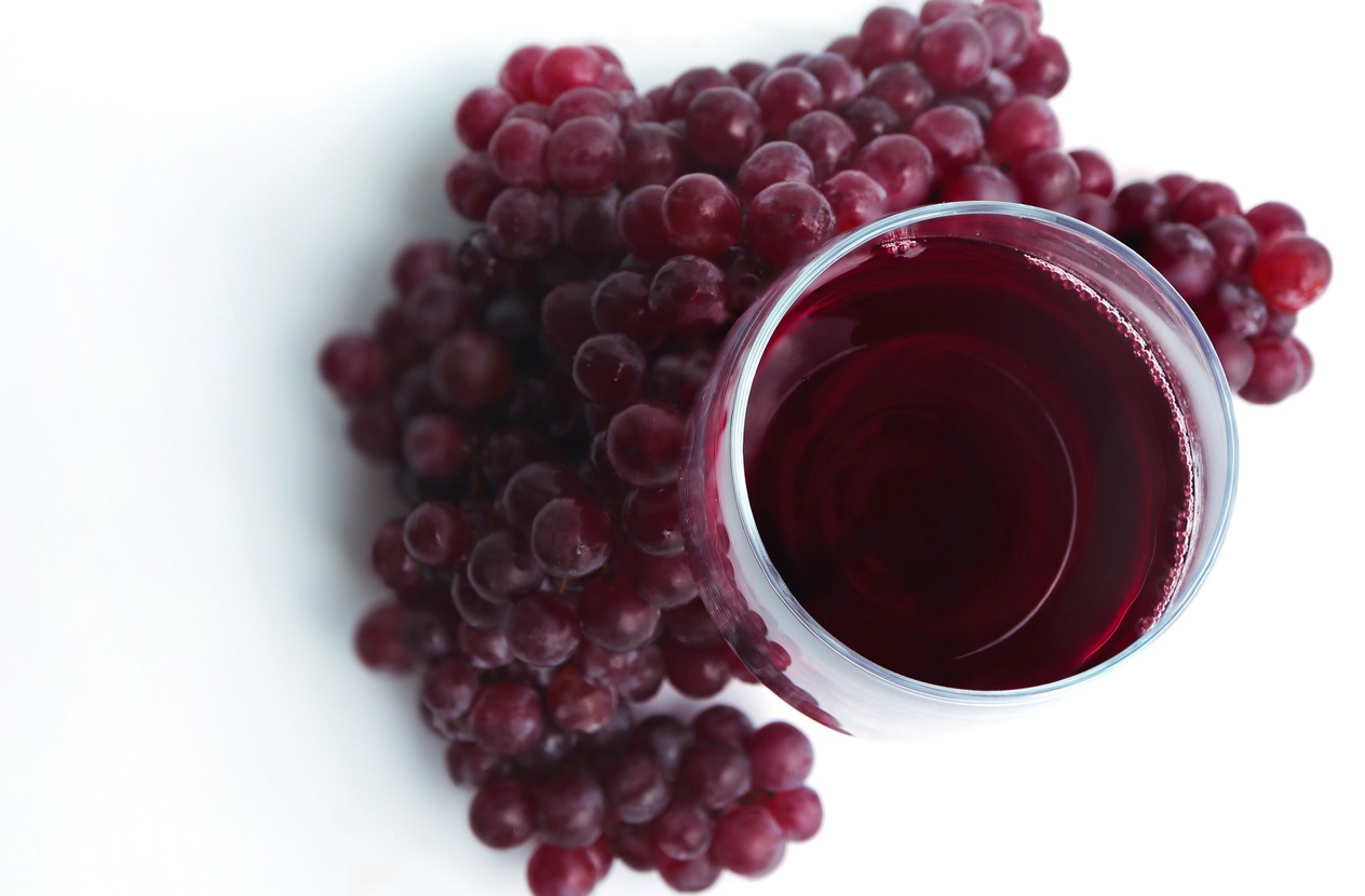Glasses of red wine and grapes on white background