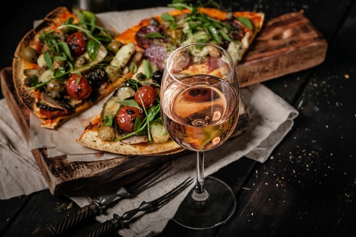 Glass of rose wine and pizza with mushrooms, eggplants, tomatoes, capers and fresh herbs on a cutting board. Copy space