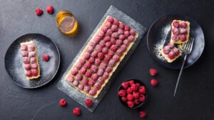 Raspberry tart with vanilla custard and white chocolate on slate board