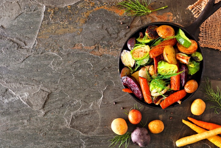 Cast iron skillet of roasted autumn vegetables, above view side border on a dark slate background