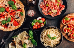 Full table of italian meals on plates Pizza, pasta, ravioli, carpaccio. caprese salad and tomato bruschetta