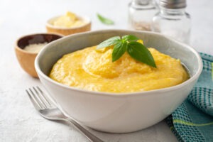 Polenta with butter and parmesan cheese in bowl on concrete background