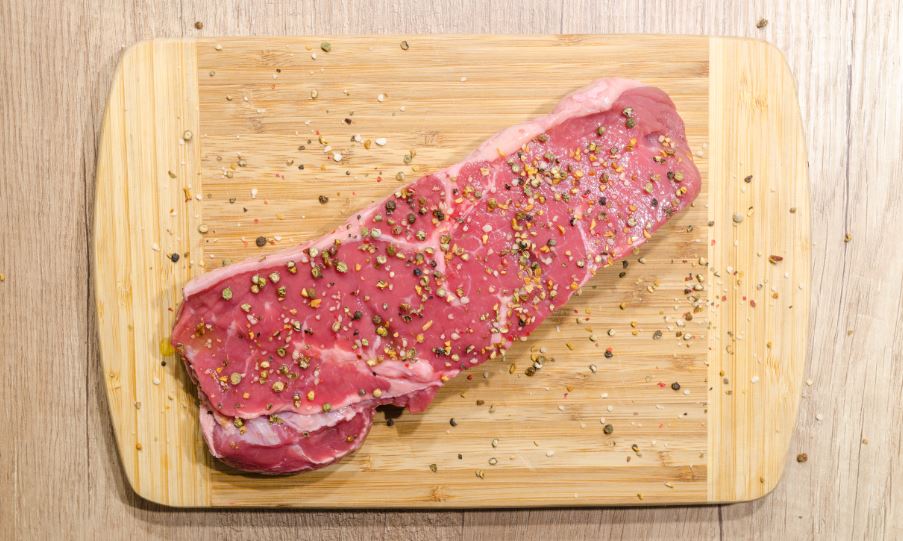 A slice of beef on top of the chopping board