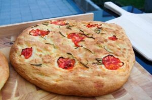 a whole focaccia bread with herbs and tomatoes