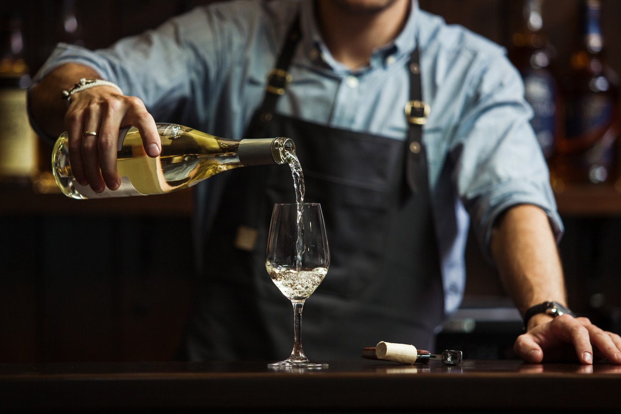 Male sommelier pouring white wine into long-stemmed wineglasses
