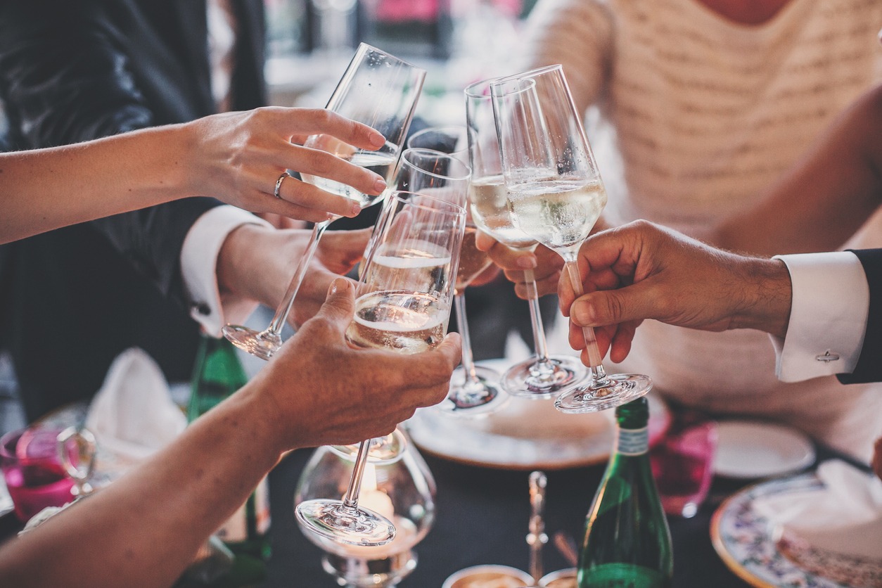 People hands toasting with champagne glasses at delicious feast outdoors in the evening