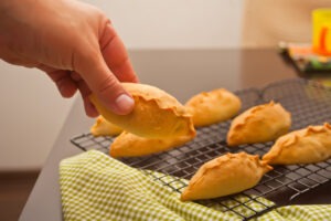Man's hand take a homemade delicious rustic pastries fresh pies with meat and potato from the metal baking rack