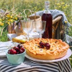 Table view served with beautiful vintage wine glasses, plates, silver cutlery and tableware, tablecloth, sweet cherry pie and fresh cherries still life. Homemade baking and recipes illustration.