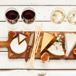 red and white wine and different kinds of cheeses on a cheeseboard on a rustic wooden table