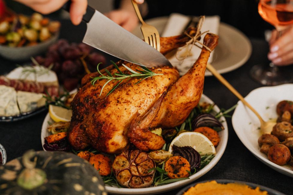 the hand of a person holding a knife to slice the chicken, other foods on the table