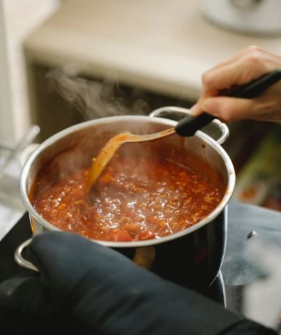 the hand of a person stirring the bolognese sauce in a saucepan